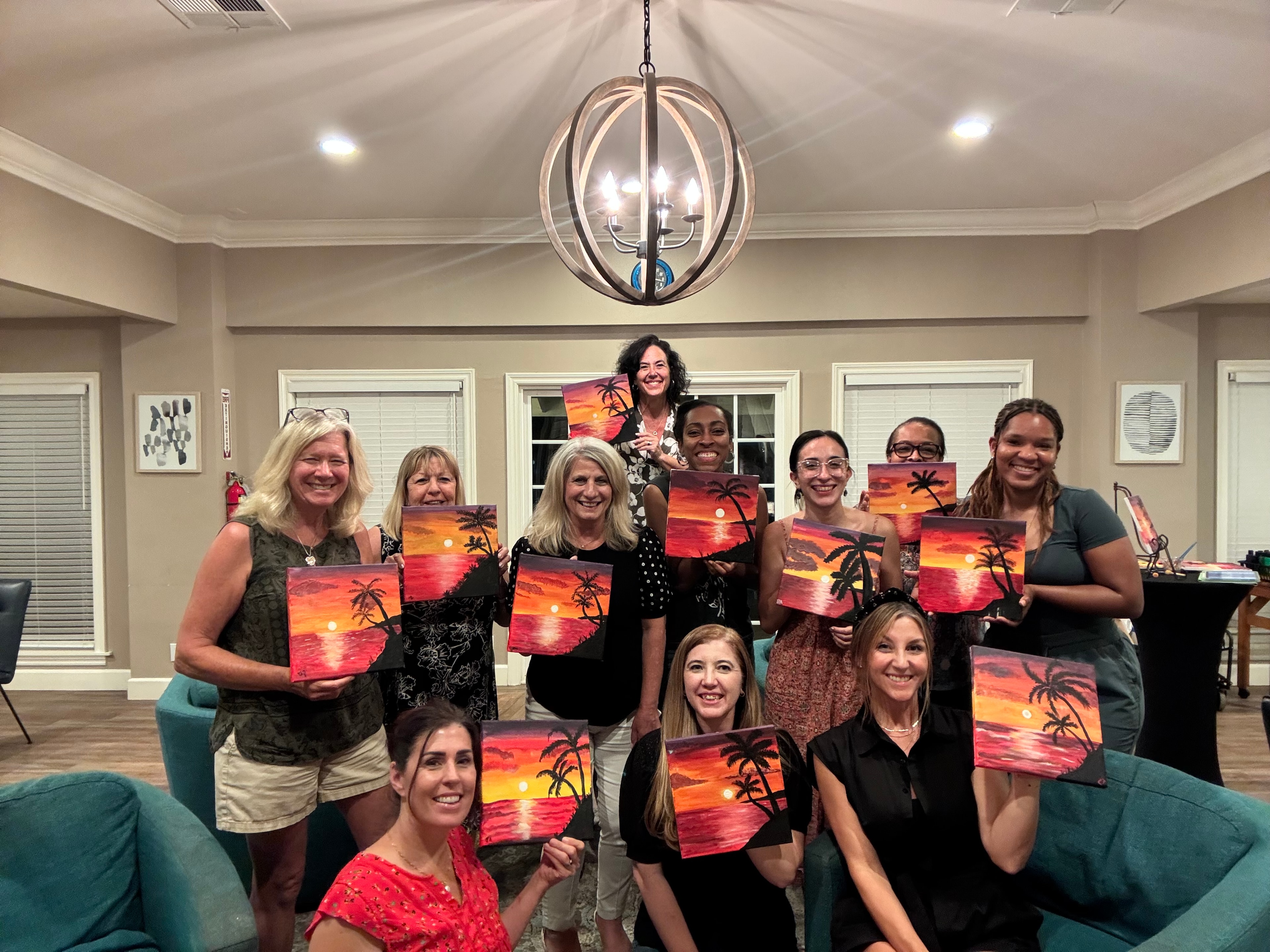 Group holding sunset palm tree paintings at Shannon Paints event
